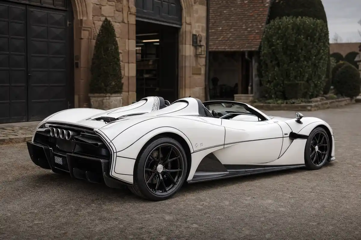 Hypercar roadster bianca con sottili linee nere, vista posteriore a tre quarti, nel cortile di un atelier in pietra