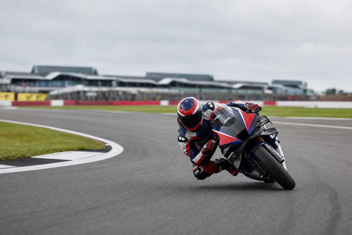 Pilota MotoGP in piega su una moto da gara mentre affronta una curva in circuito, con cielo nuvoloso