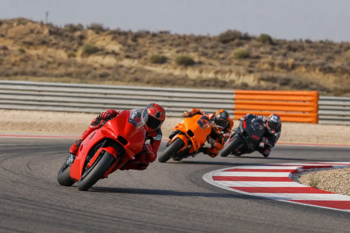 Tre moto da corsa in piega a sinistra: una rossa in testa, seguita da una arancione e una scura su circuito asfaltato