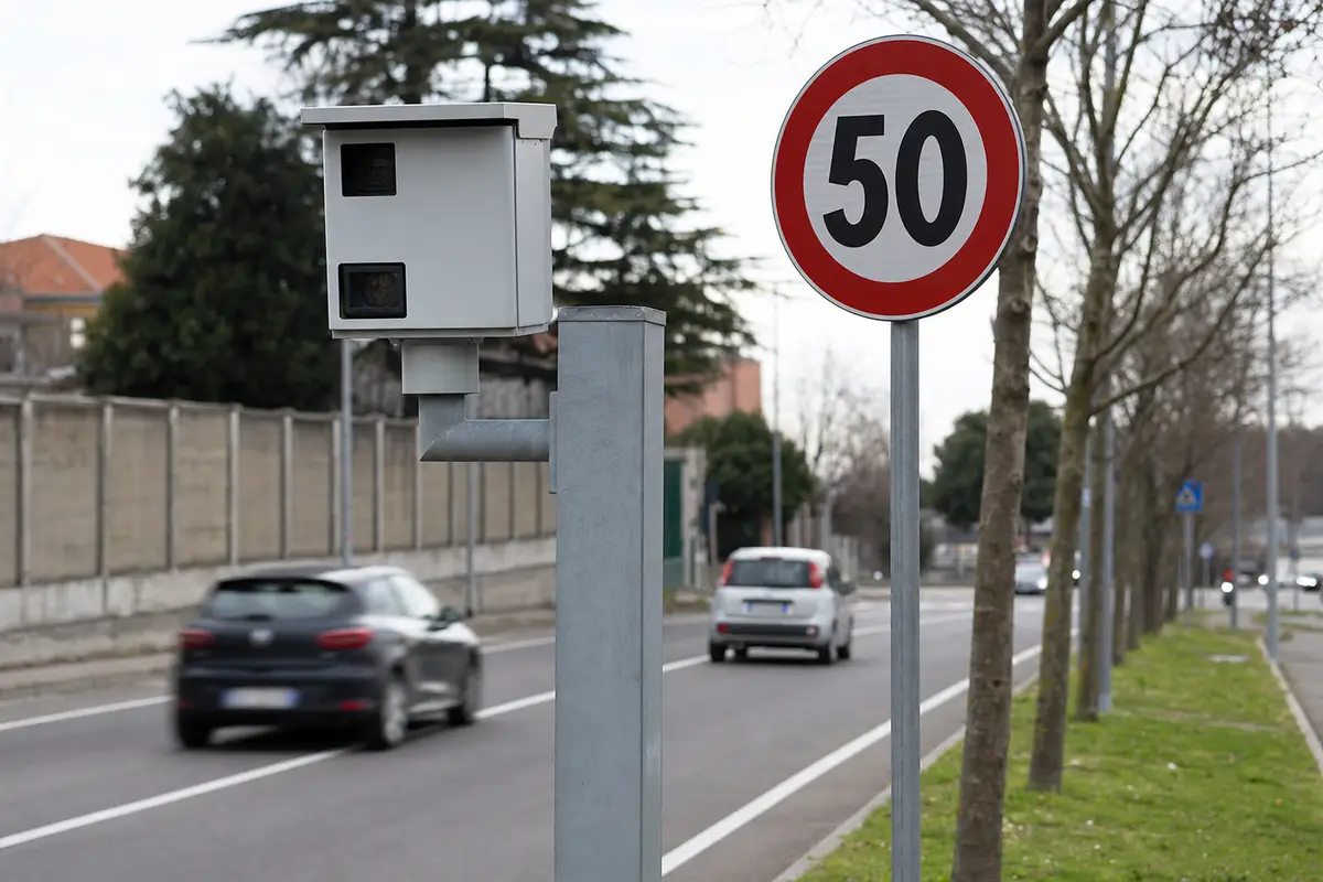 Autovelox a bordo strada con cartello del limite 50 km/h e auto in transito su una strada urbana