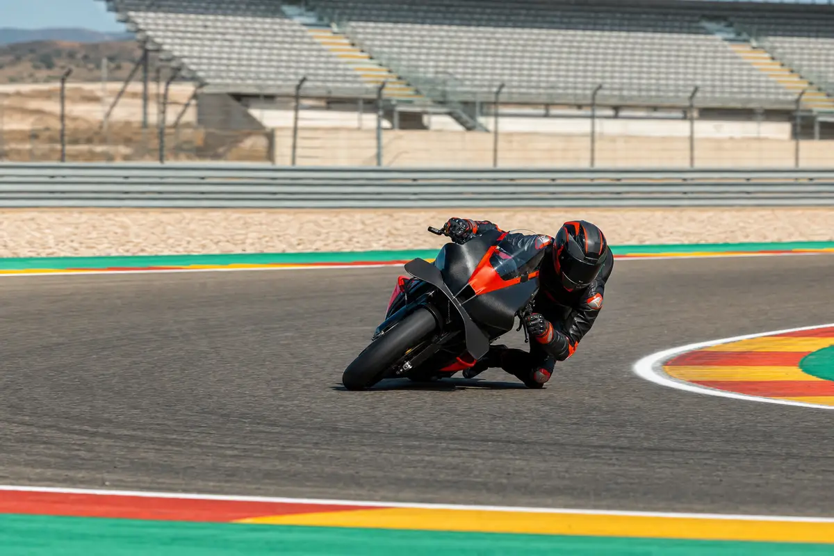 Pilota in tuta nera e rossa in piega estrema su moto da gara, in curva su circuito con cordoli colorati