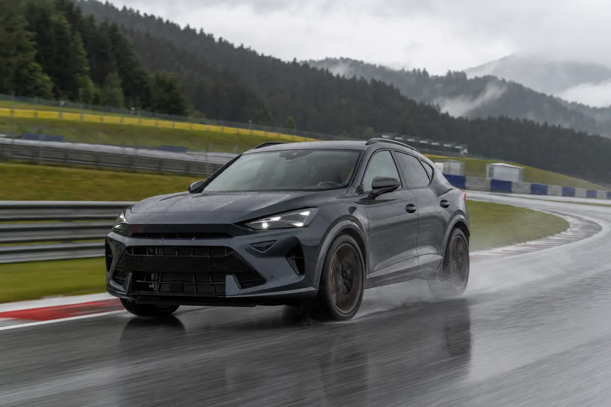 Crossover sportiva grigio scuro in curva su pista bagnata, con spray d’acqua e cordoli rossi e bianchi