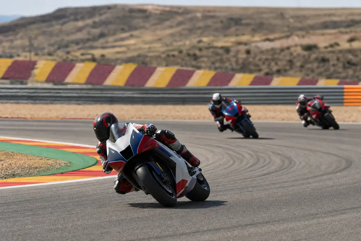 Tre moto da corsa piegate in curva su un circuito, con pilota in primo piano e due inseguitori sullo sfondo