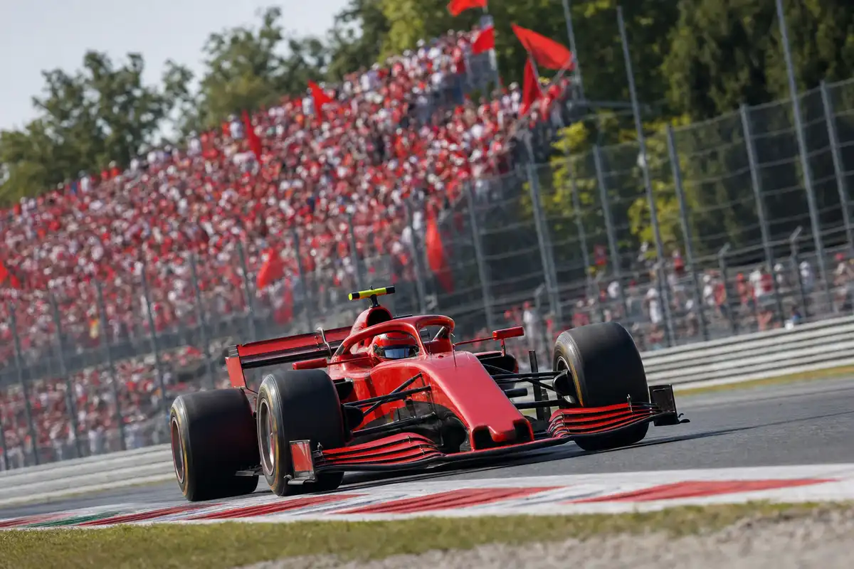 Monoposto rossa in curva su cordoli rosso-bianchi davanti a tribune piene di tifosi in rosso con bandiere