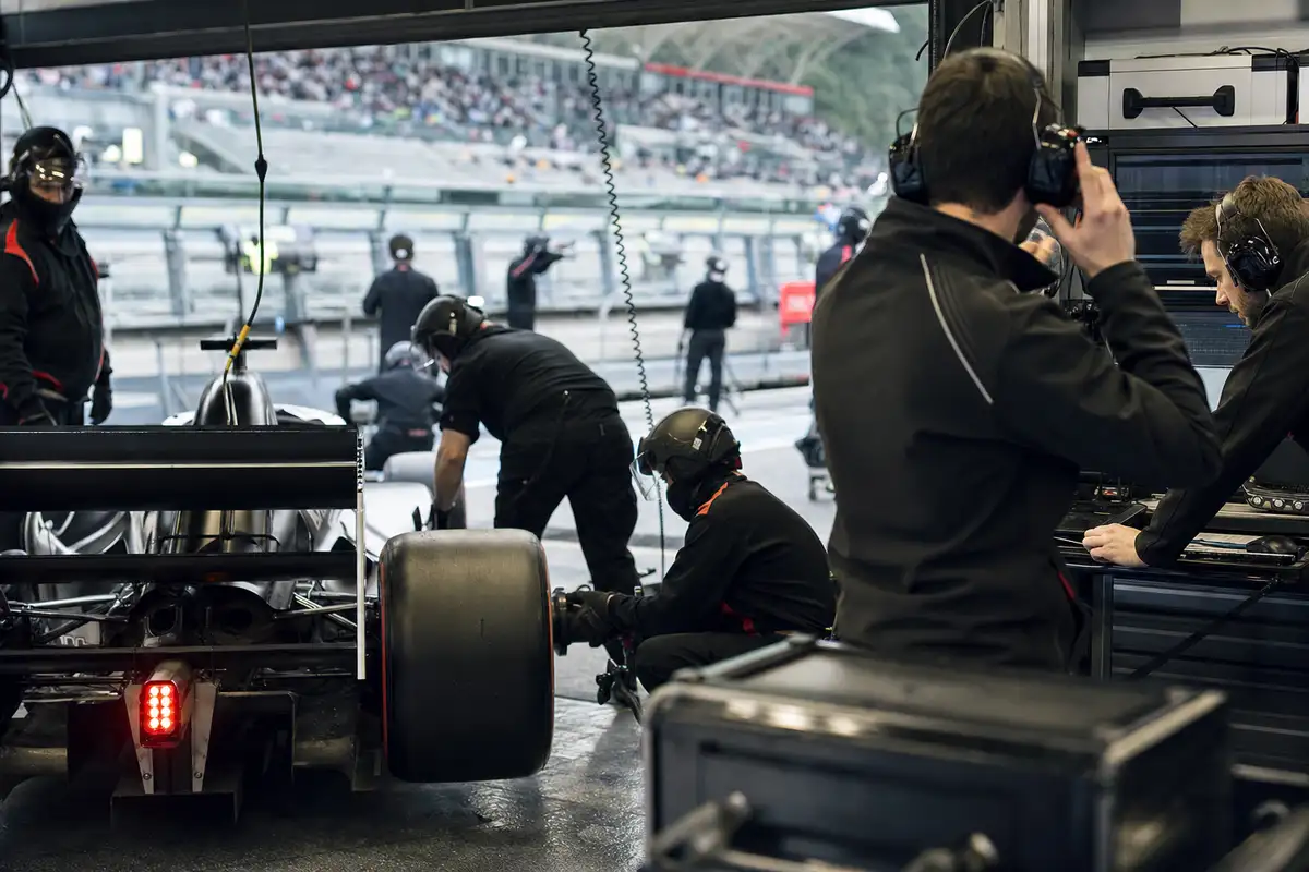 Meccanici al lavoro su una monoposto in pit lane, con pneumatici e monitor dati durante un weekend di gara
