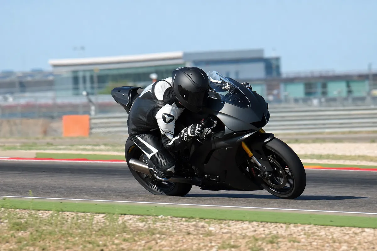 Pilota in tuta nera su moto da gara nera piegato in curva su circuito asfaltato con cielo sereno