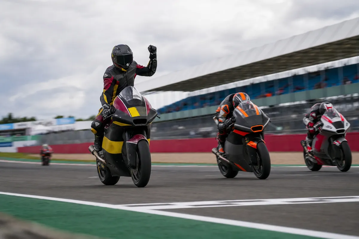 Pilota in moto alza il braccio in segno di esultanza mentre due rivali lo superano sul rettilineo