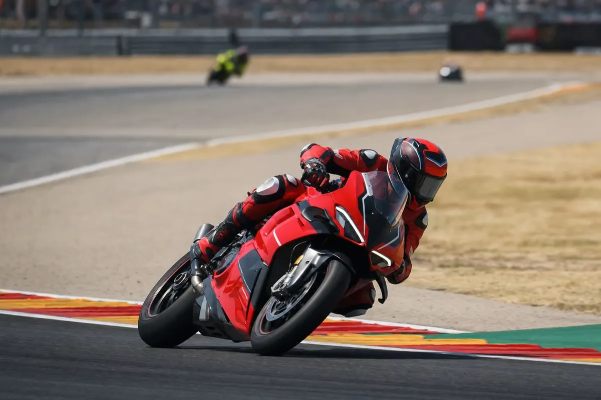 Pilota di MotoGP su moto rossa in piega estrema su una curva del circuito, con sfondo mosso