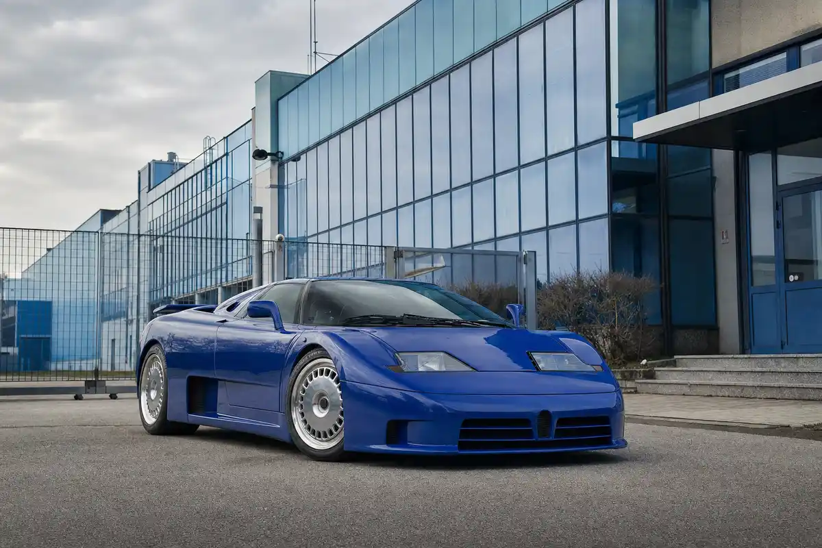 Supercar blu anni Novanta parcheggiata davanti a un edificio industriale con facciata in vetro azzurro