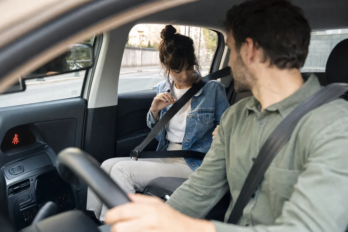Passeggera sul sedile posteriore allaccia la cintura mentre il conducente si gira a controllare