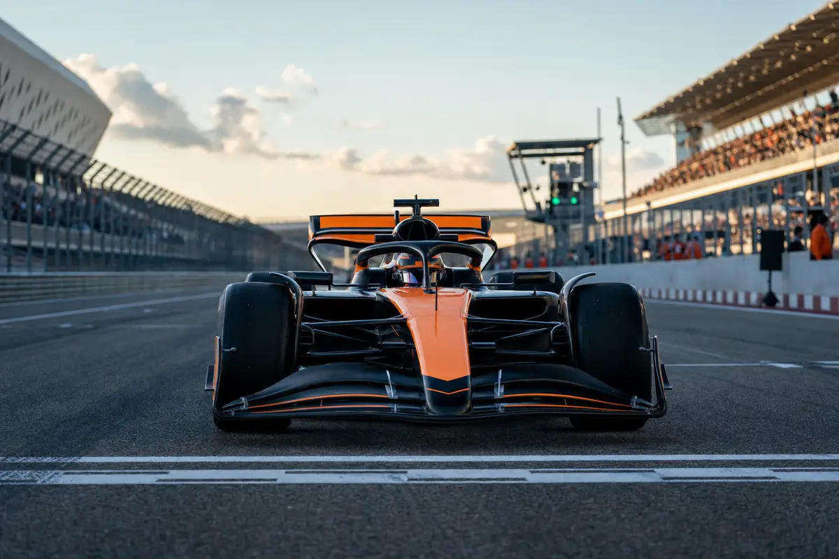 Monoposto arancione e nera ferma sulla casella della pole position sulla griglia di partenza, con tribune sullo sfondo