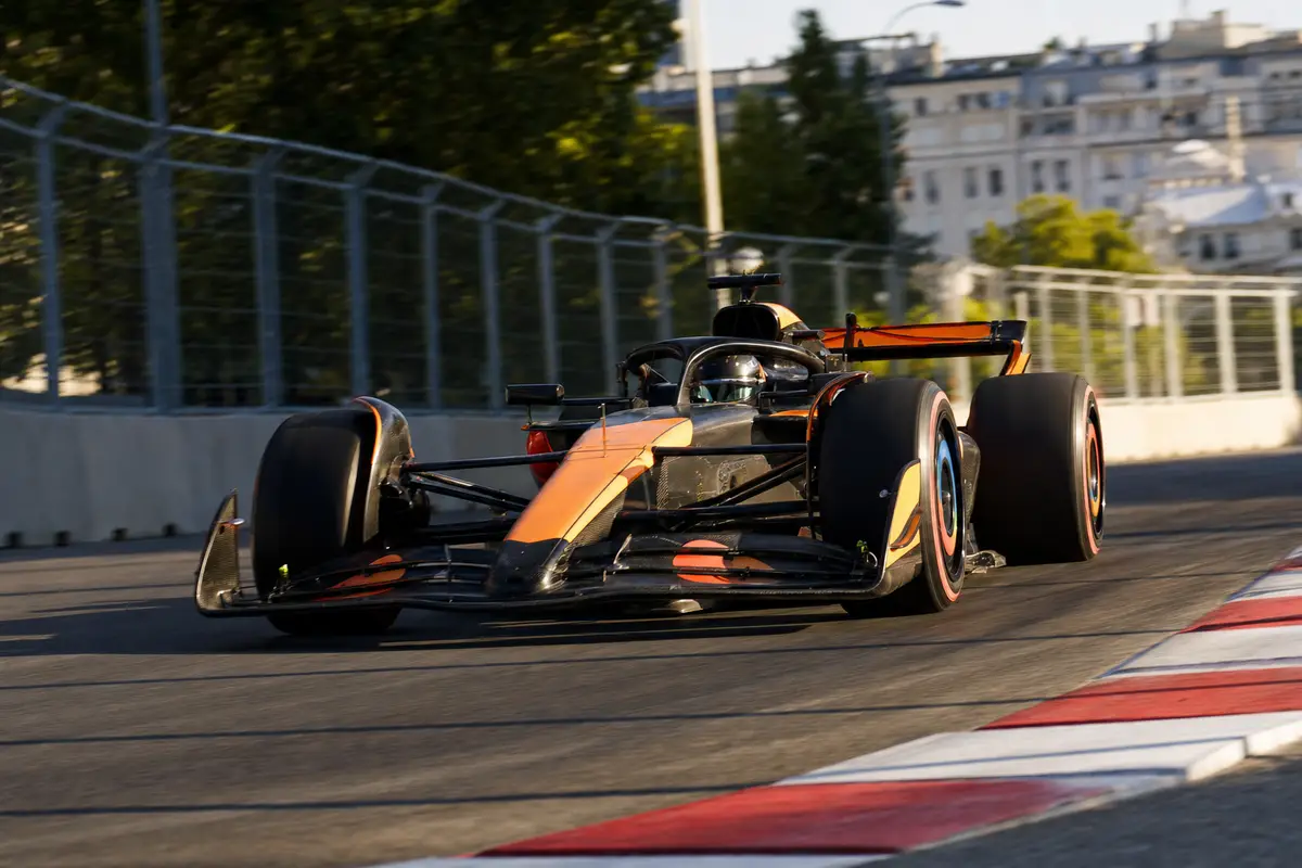 Monoposto di Formula 1 arancione e nera in uscita da una curva su circuito cittadino, con cordoli rosso-bianchi
