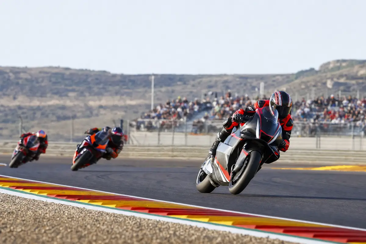 Moto da corsa in piega su una curva del circuito, con due inseguitori sfocati e tribune sullo sfondo