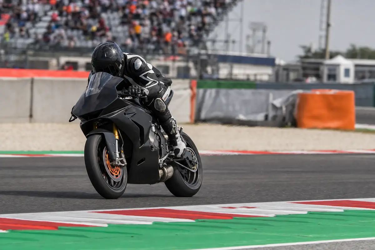 Pilota in tuta nera in forte frenata su moto da gara, vicino ai cordoli tricolore in circuito