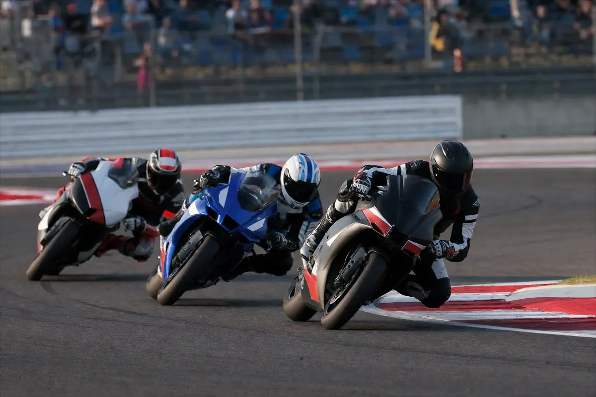 Tre piloti in moto piegati in curva su un circuito, in lotta ravvicinata con cordoli rossi e bianchi